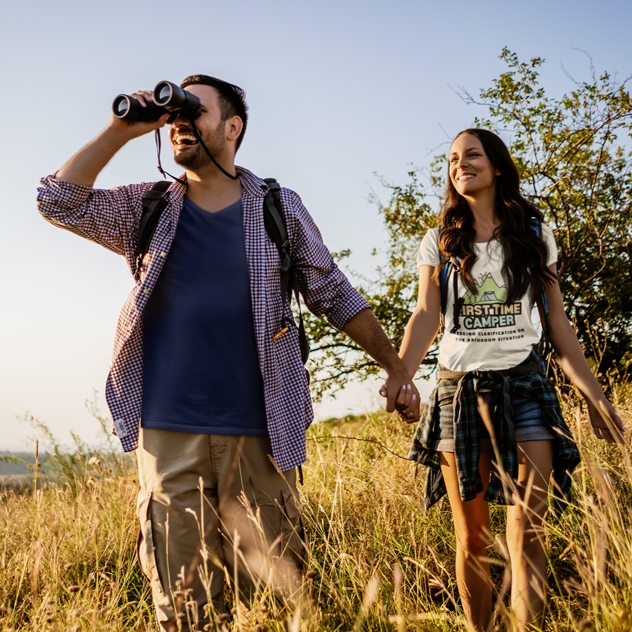 Man and woman walking through a field with binoculars and backpacks.