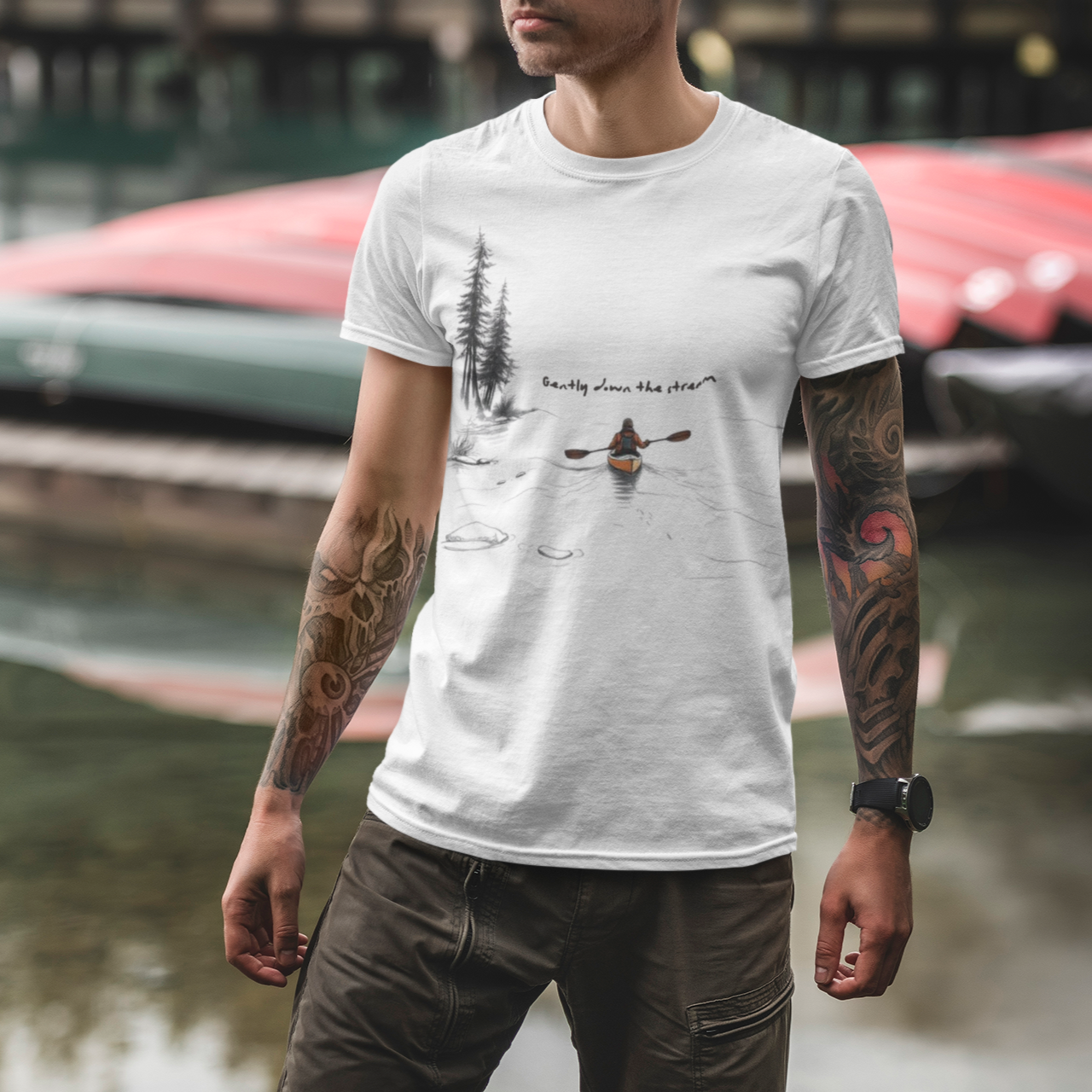 Man wearing a white t-shirt with a kayak and canoe design by a body of water.
