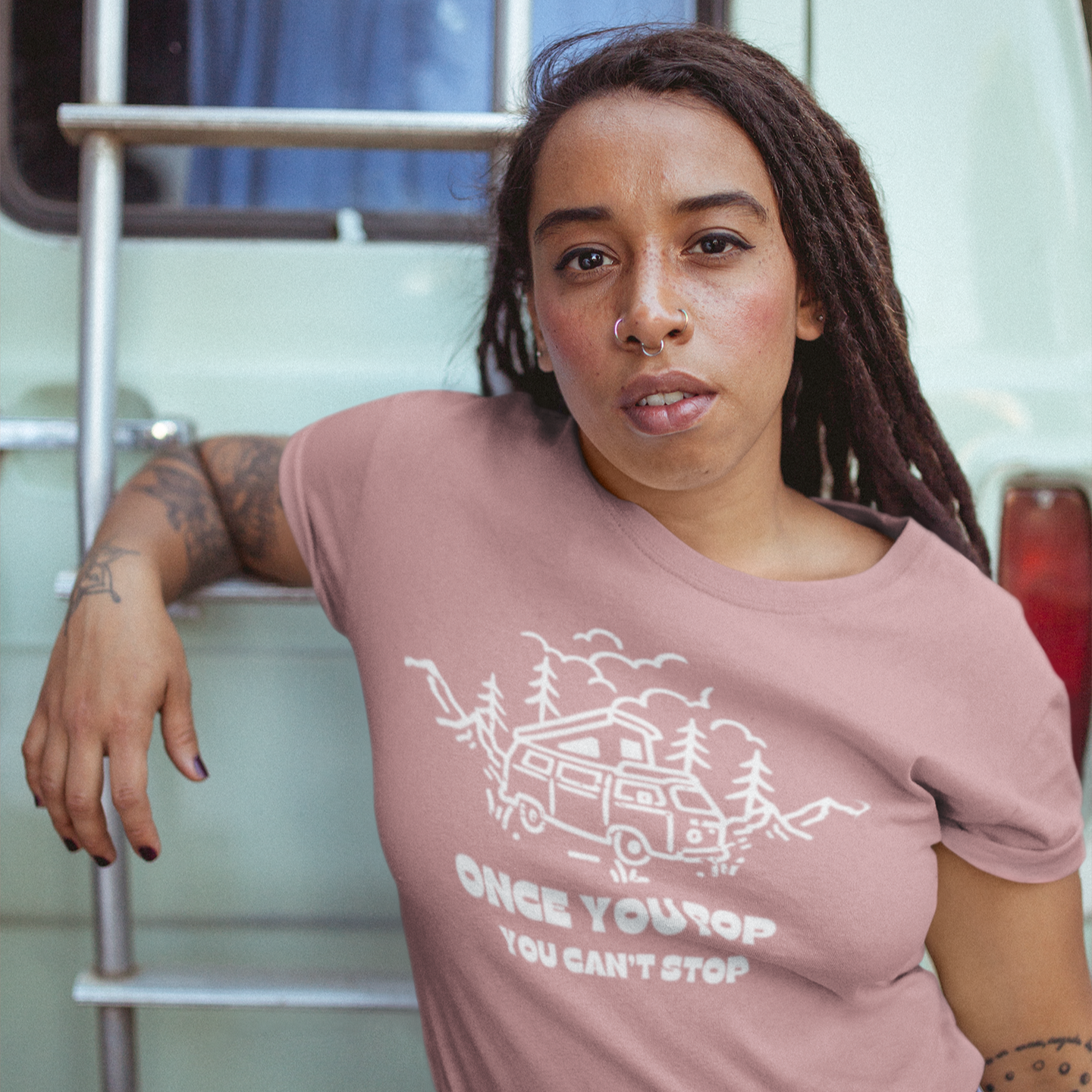 Person wearing a pink t-shirt with a graphic design and text, standing inside a vehicle.