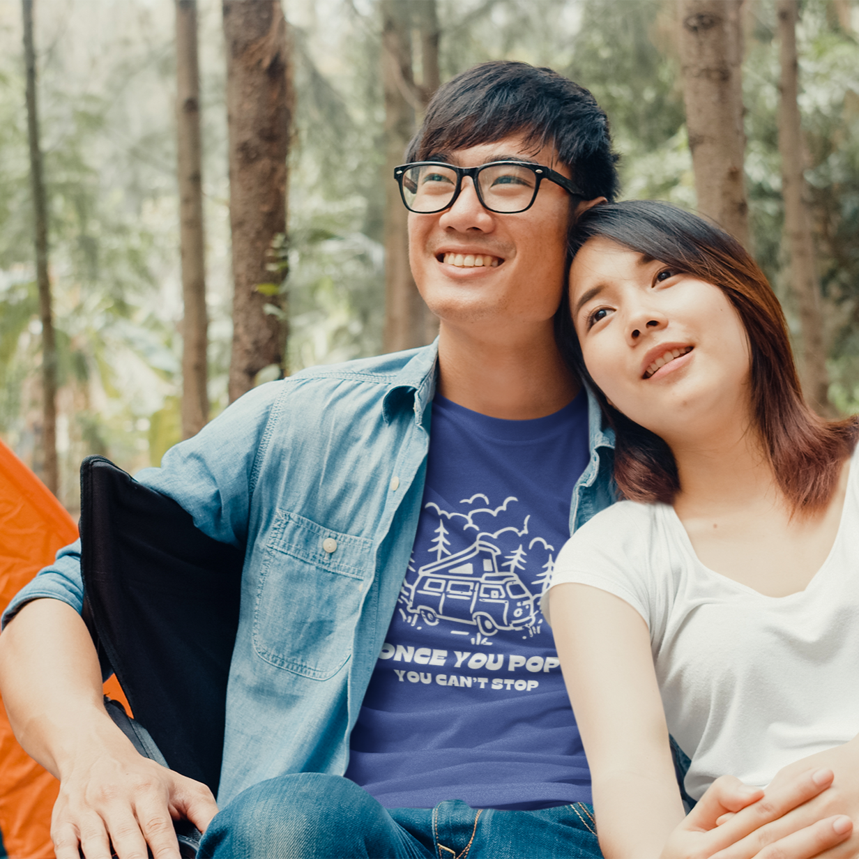Two people sitting together in a forest setting with camping gear.
