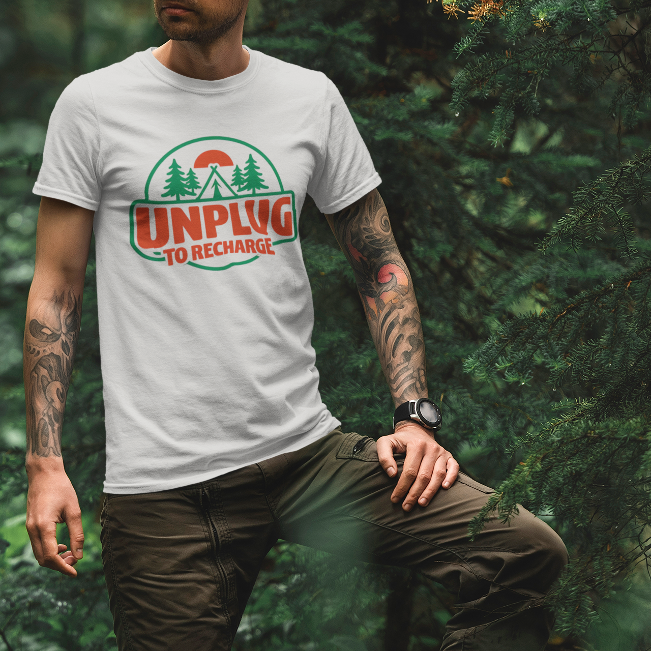 Person wearing a white t-shirt with a Unplug to Recharge graphic design in a forest setting