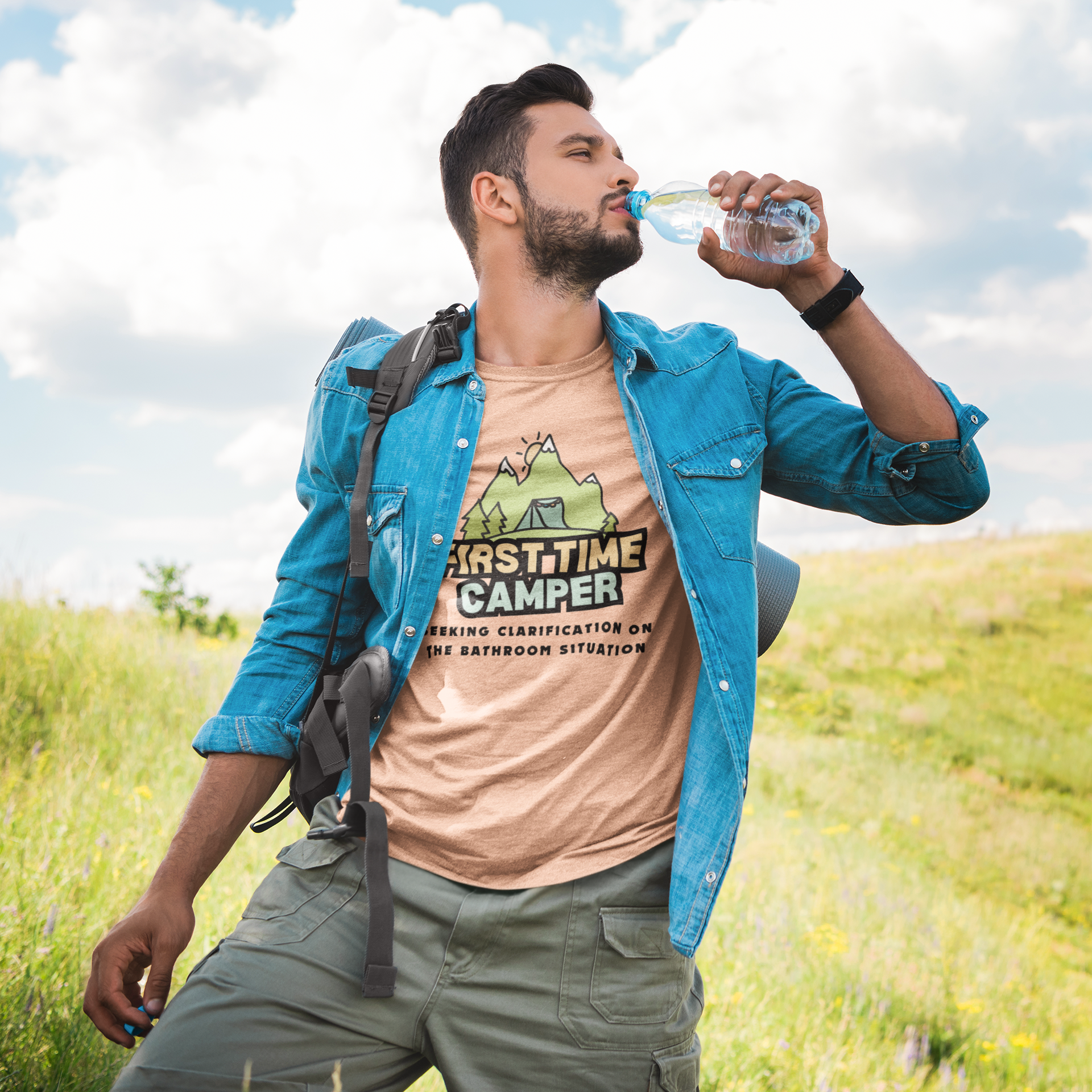 Man in a field wearing a 'First Time Camper' t-shirt, drinking water.