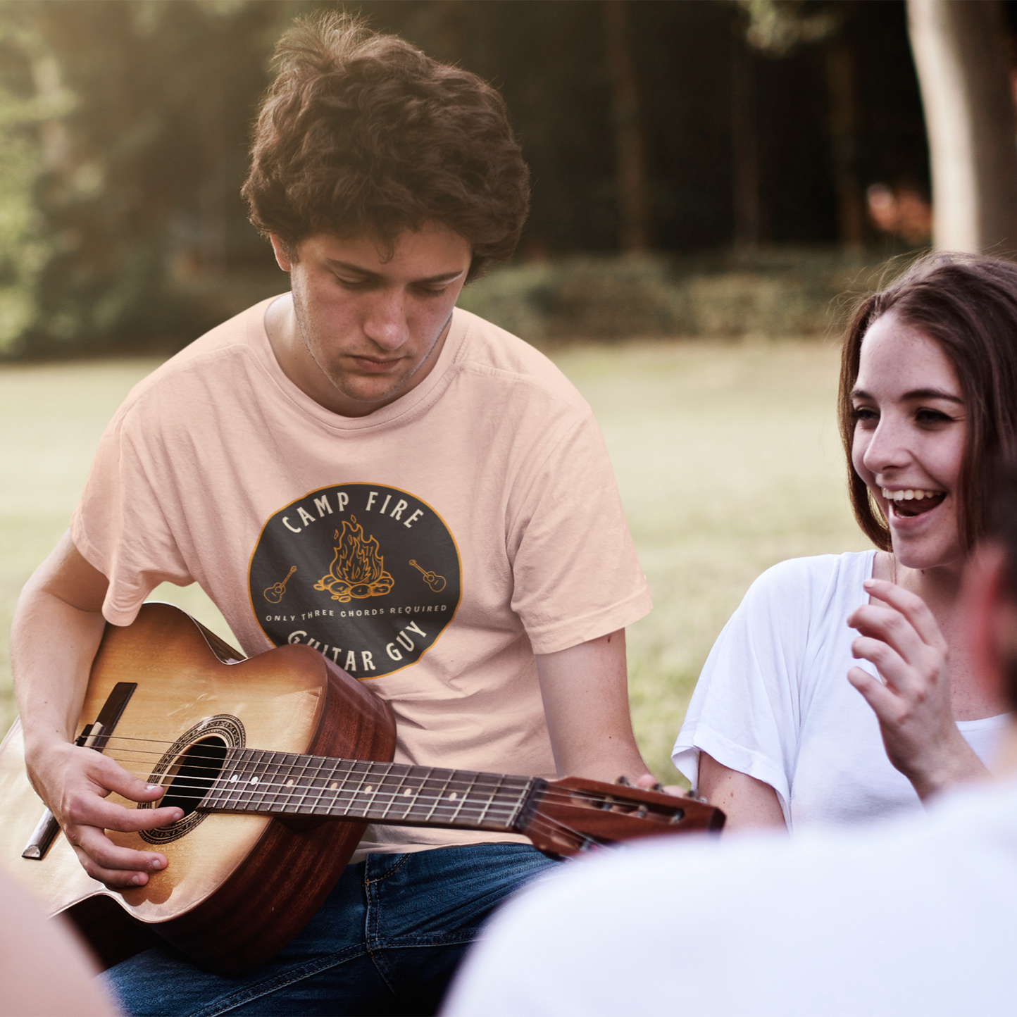 Person playing guitar with others in a park setting