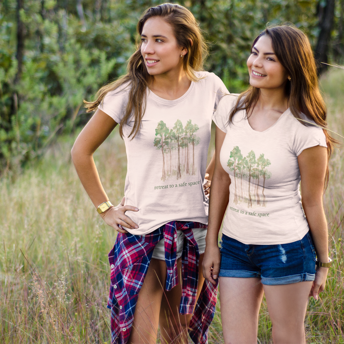 Two women standing in a field wearing matching t-shirts that say Retreat to a Safe Space with a forest design.